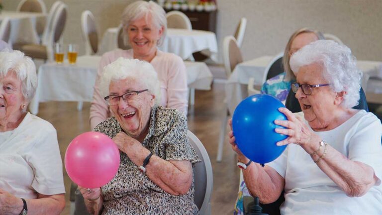 Older adult arranging family photos and a favorite chair in a comfortable assisted living room.